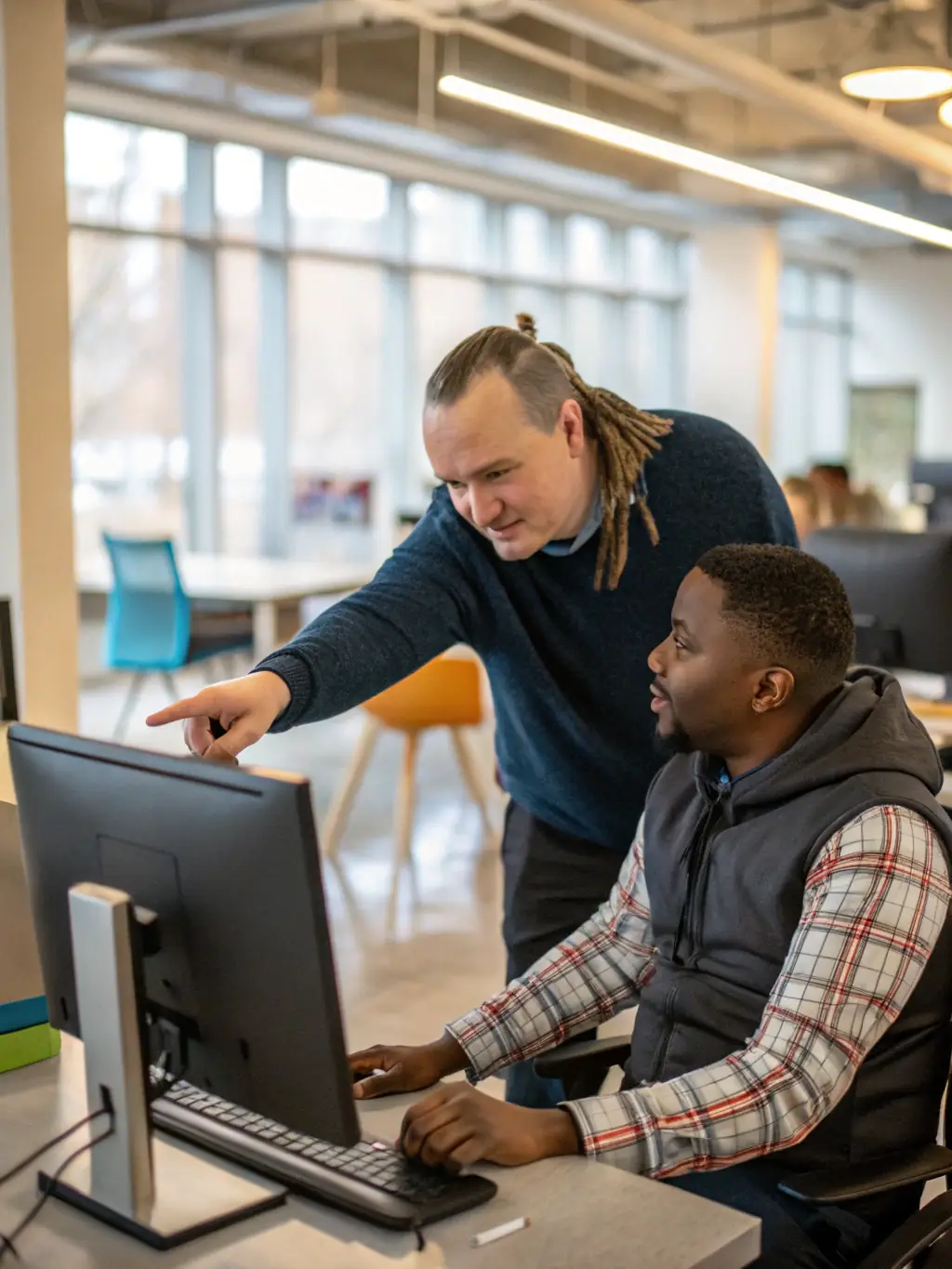 A young adult with Down syndrome working on a computer with assistance from a job coach, in a modern office environment, showcasing ADAPEI's supported employment program.